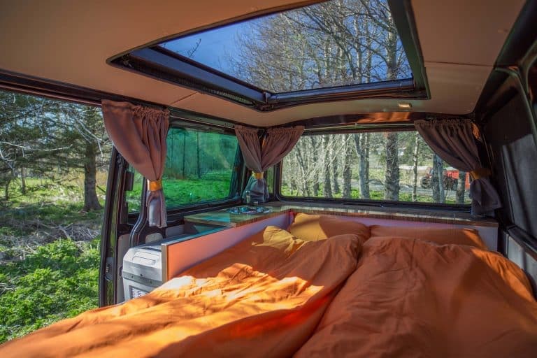 Made-up double bed in mustard-orange bedding inside the Highlander I Budget, sky roof open above and curtains tied back with gold ribbon