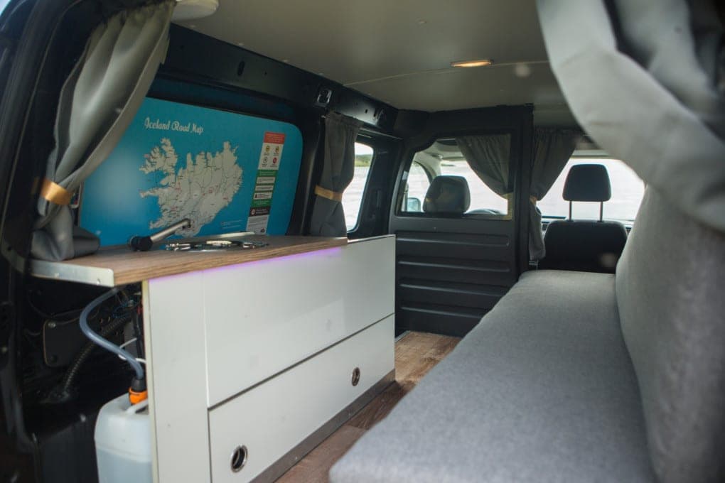 Fold-out kitchen unit in the budget Caddy with a two-burner hob, wood-look counter and water jug, Iceland road map on the rear door