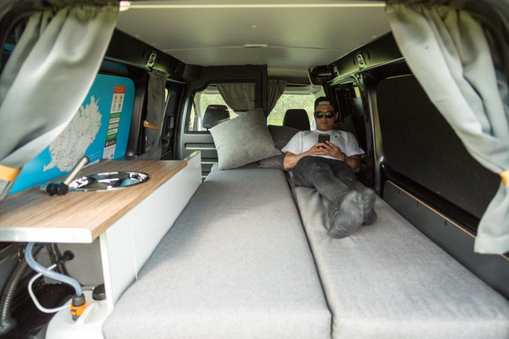 Made-up bed in the back of the budget Caddy with a grey pillow and Iceland road map decal on the rear door