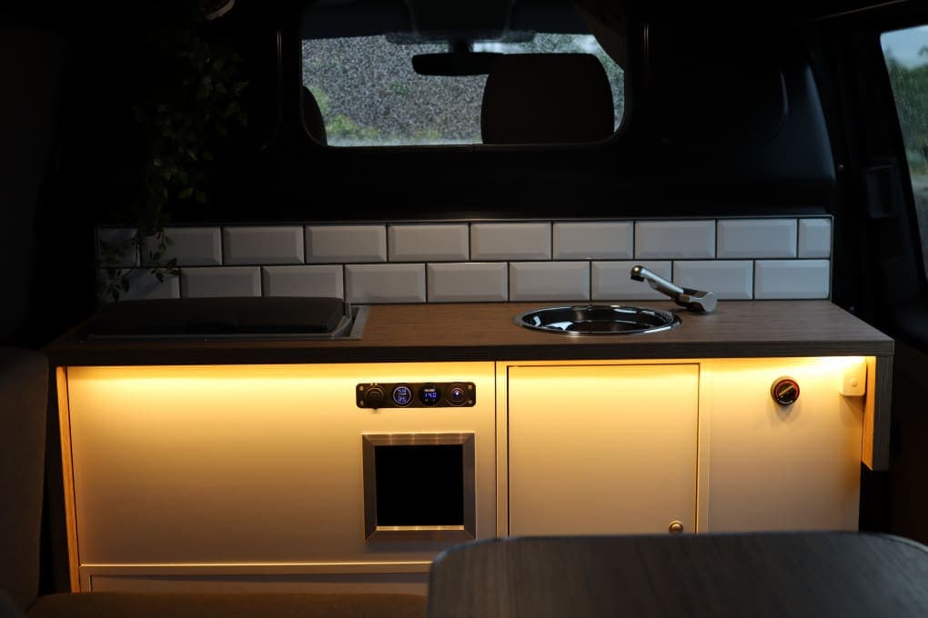 Close-up of the galley countertop with round sink, fold-up single-burner stove and white subway-tile backsplash, LED strip lighting underneath