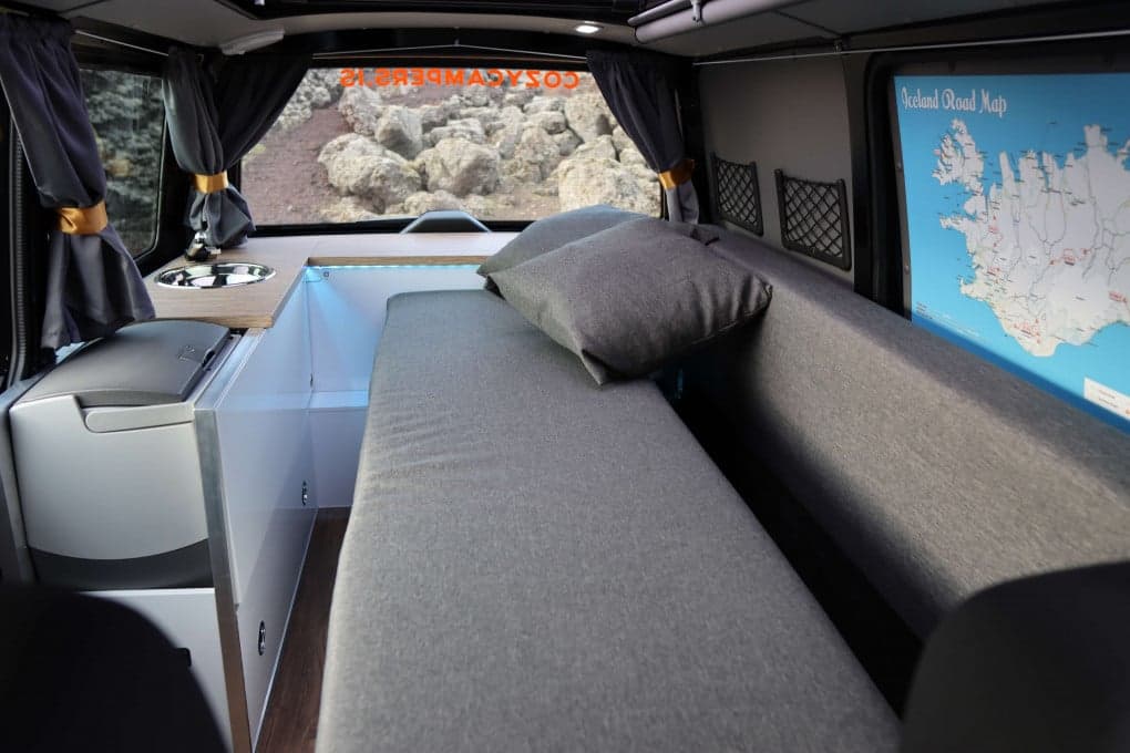 Interior of the Highlander II with the full-length gray rear bench flattened into a single sleeping platform and one pillow at the head end