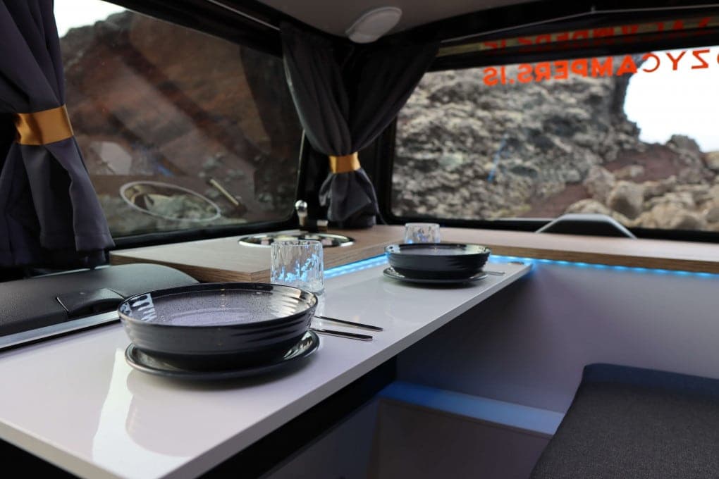 Two place settings with plates, cutlery and glasses on the fold-out table in the Highlander I, lava rock visible through the rear window