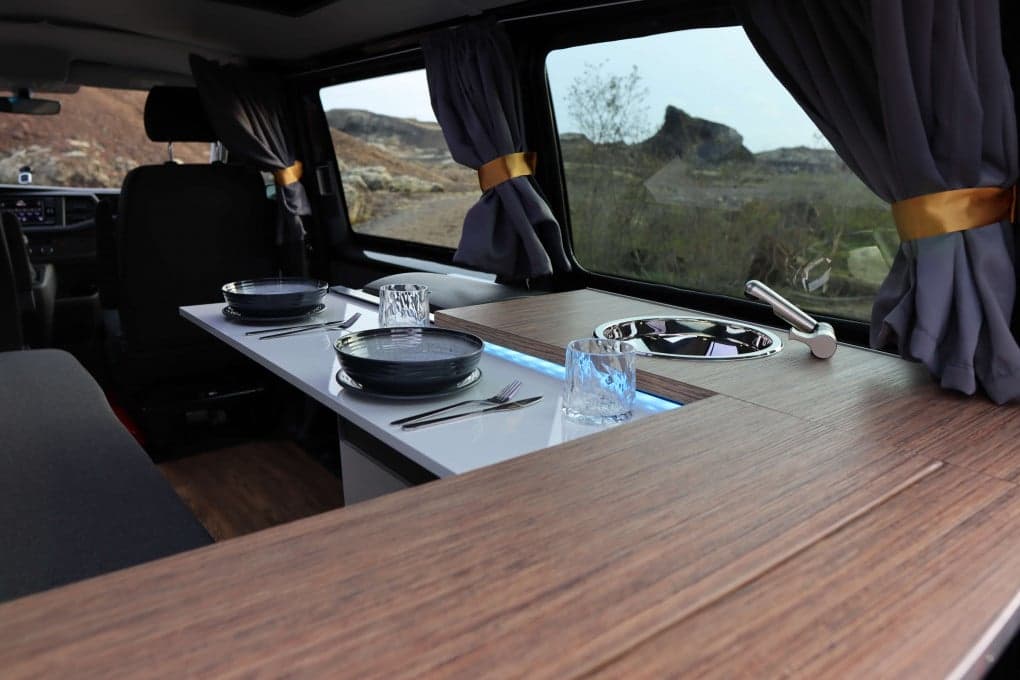 Wood-look galley counter with a round stainless sink, faucet and two place settings, front seats visible ahead through the cabin