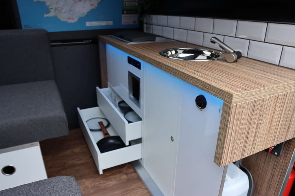 Open drawer in the Highlander III galley showing stacked plates and a frying pan beside the sink and wood-look countertop