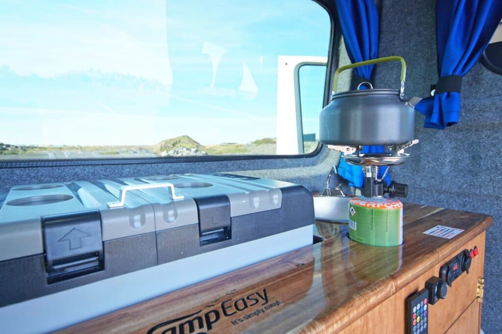 Kettle on a gas burner on the Easy Viking's counter, with a water container and a green landscape through the window