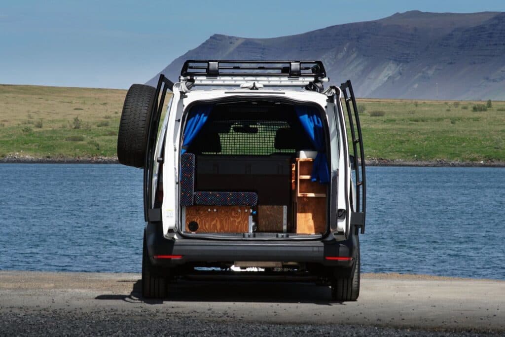 Rear doors of the Easy Ranger open beside a fjord, spare wheel mounted on the door and wooden units inside