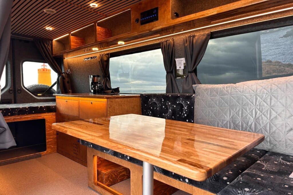 Large polished wooden table between bench seats in the Easy Luxury, with the galley and coffee machine behind