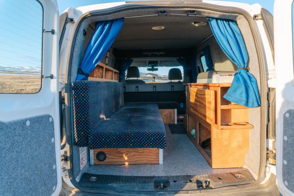 Side door open on the Easy Small showing the bench seat, wooden galley unit and bright blue curtains