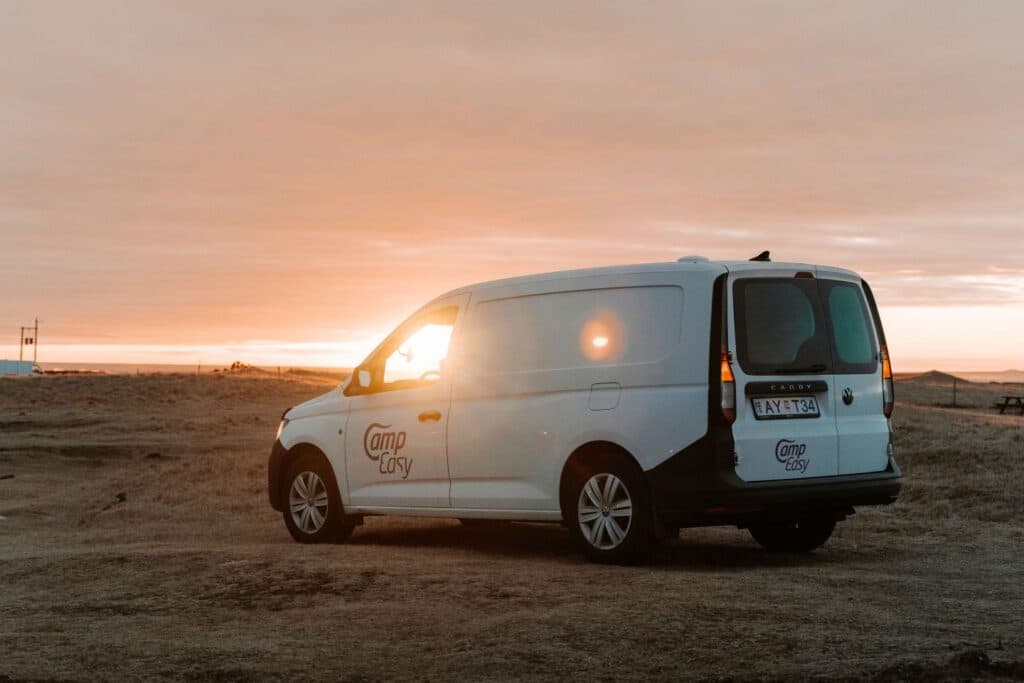 White VW Caddy Maxi camper at sunset with its interior light on, parked on open ground
