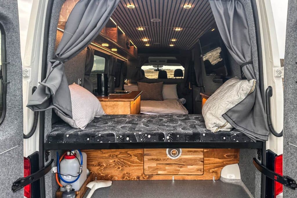 Rear doors of the Easy Monster open showing two berths with pillows, a wooden drawer unit and a water container