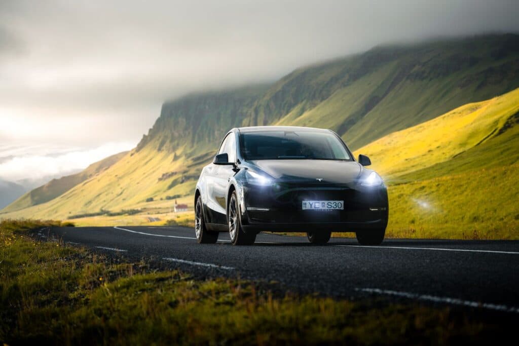 Dark Tesla Model Y on a road running below a steep green Icelandic mountainside