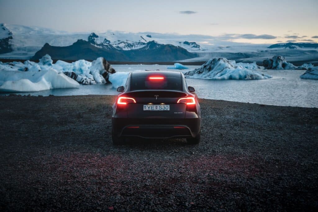 Rear of a dark Tesla Model Y parked at a glacier lagoon full of icebergs