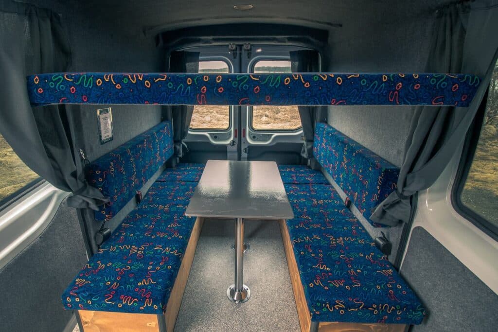 Upper bunk board folded above facing bench seats and a table inside the Easy Big