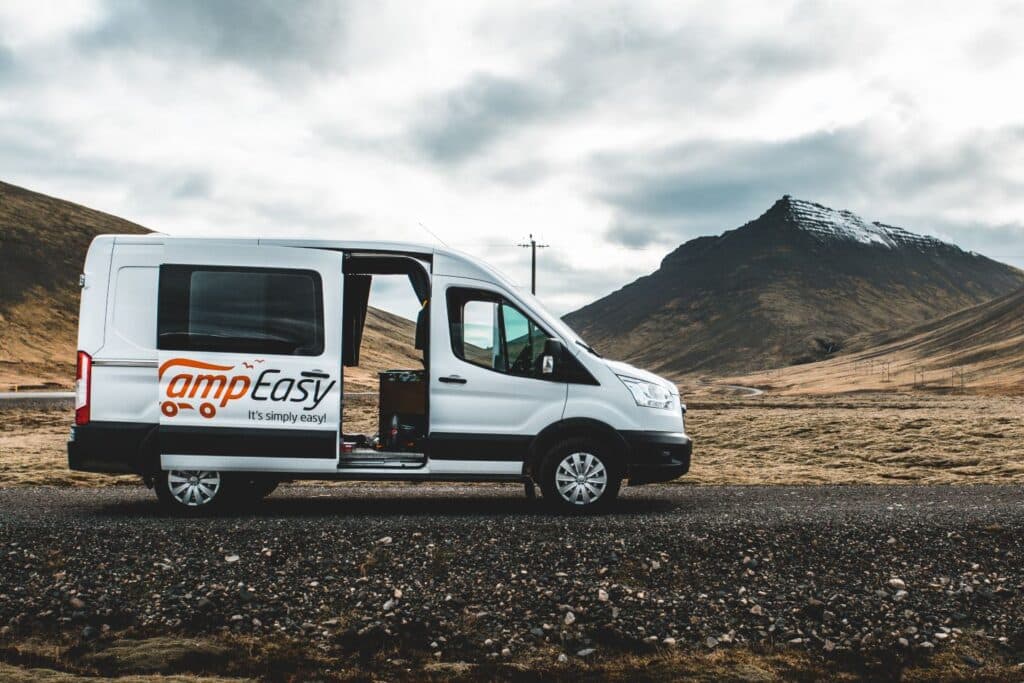 White Ford Transit camper with its side door open on brown moorland below a dark peak