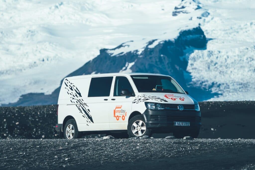 White VW Transporter 4x4 camper parked on a black beach in front of a stranded iceberg