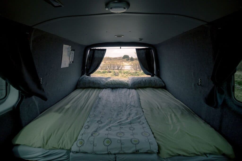 Bed made up with a green sleeping bag inside the Easy Clever EXP, rear window looking onto scrubland