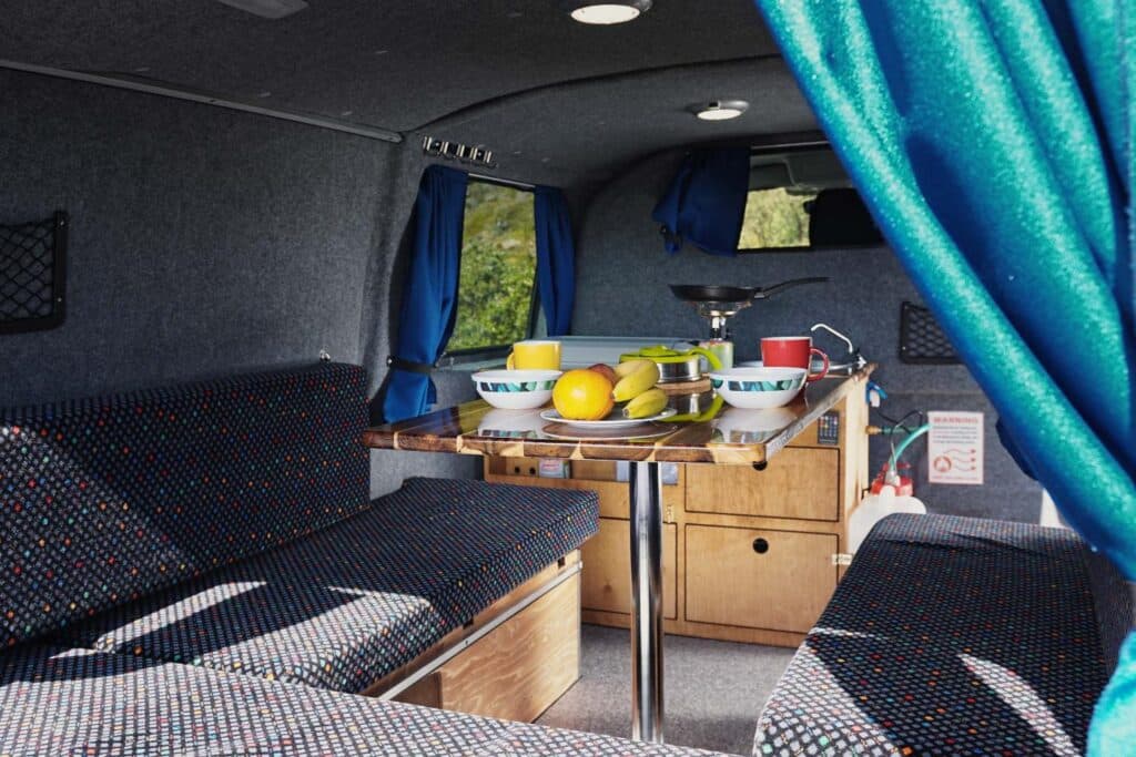 Interior of the Easy Clever with bench seats, a wooden table holding fruit bowls and turquoise curtains