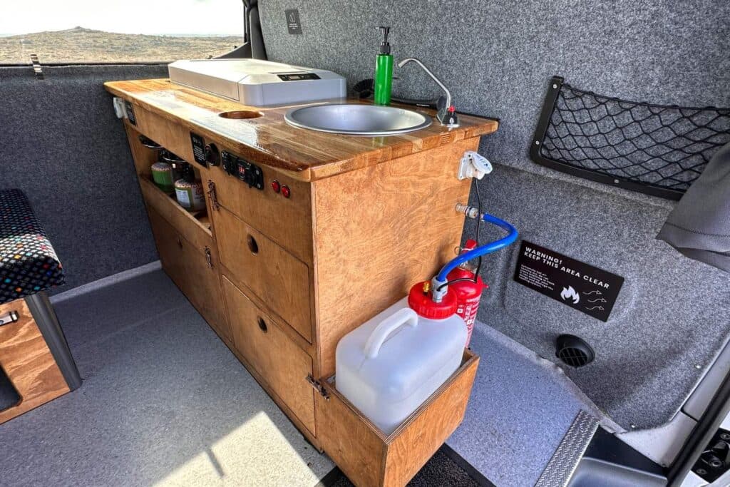 Wooden galley unit in the Easy Auto with a stainless sink, cool box on the worktop and a water container below