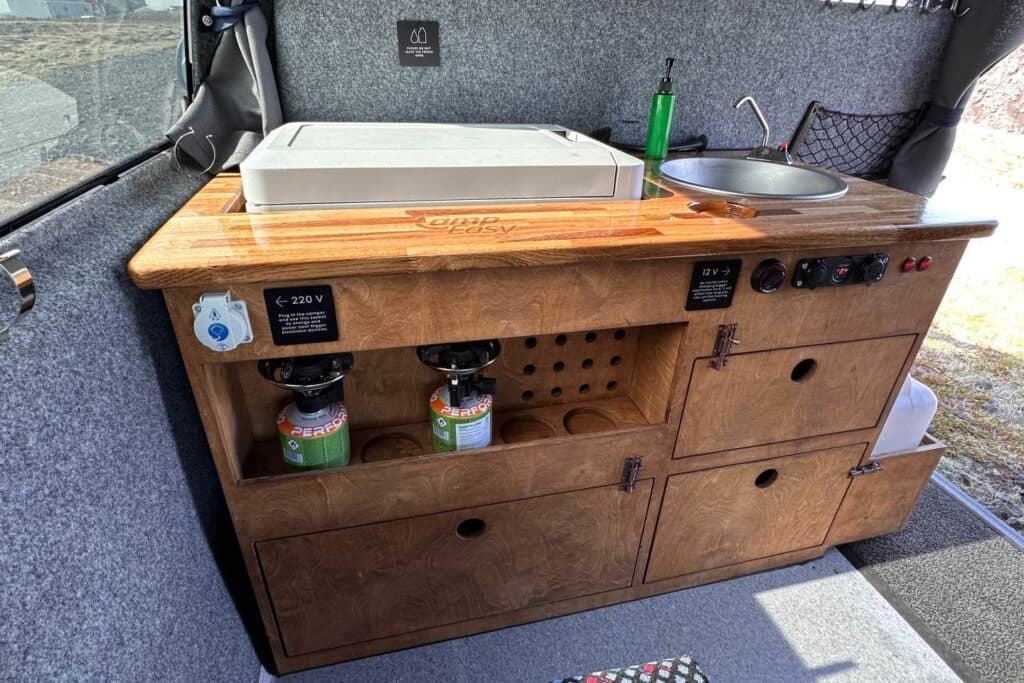 Wooden galley in the Easy Fun EXP with a cool box, sink, gas canisters and a chopping board worktop
