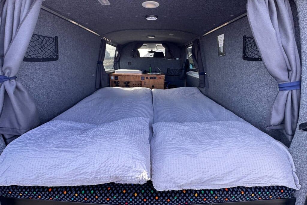 Interior of the Easy Auto with the double bed made up in white duvets and grey curtains drawn