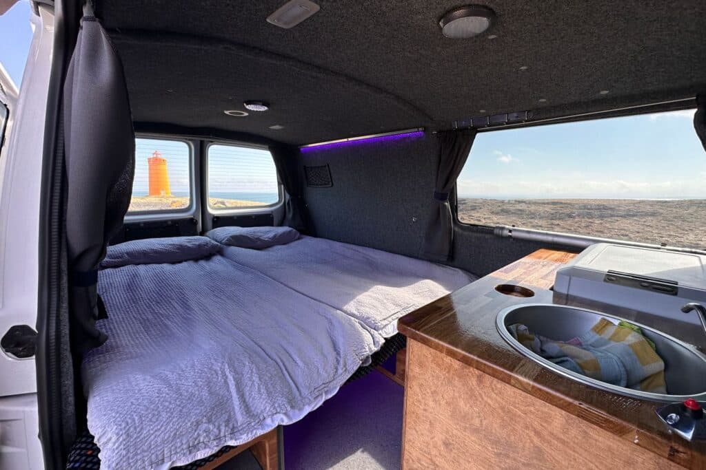 Bed made up in the Easy Fun with the galley sink in the foreground and an orange lighthouse through the window