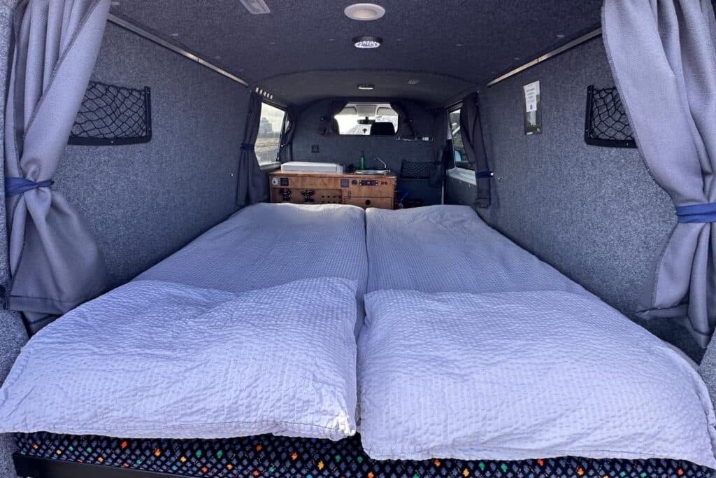 Double bed made up with white duvets inside the Easy Fun EXP, curtains tied back at the rear windows