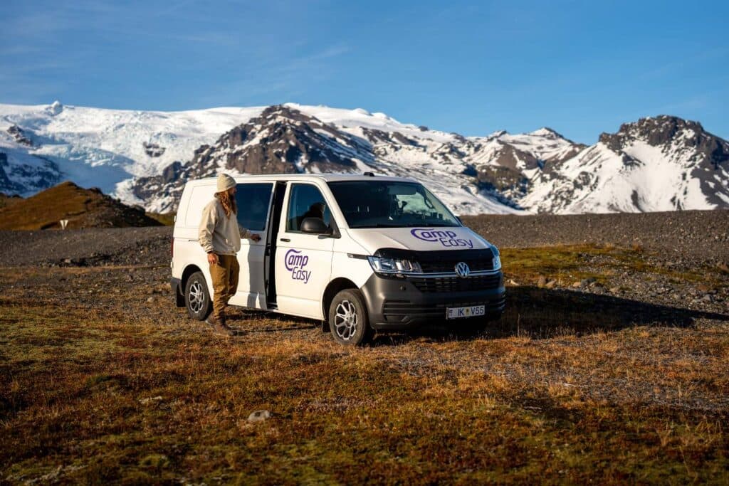 White VW Transporter camper parked on autumn tundra below a snow-covered mountain