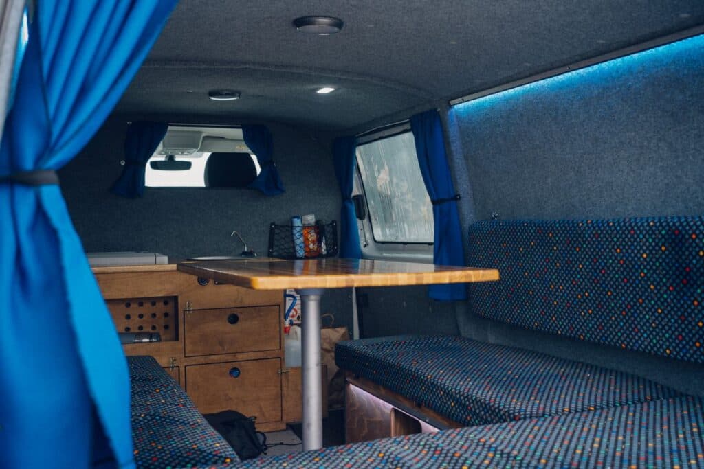 Interior of the Easy Auto EXP with the wooden table up between bench seats and blue curtains at the windows